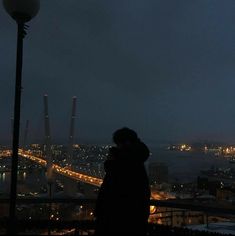 a person standing on top of a building next to a street light at night with city lights in the background