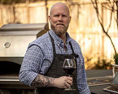 a man holding a glass of wine in front of an outdoor bbq with grill