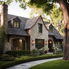 a stone house with lots of windows and bushes in front of the house is surrounded by greenery