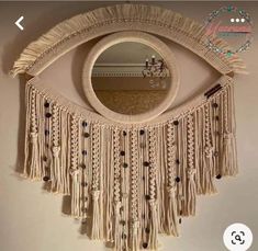 an eye shaped mirror with tassels hanging on the wall next to a shelf