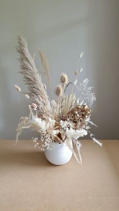 a white vase filled with dried plants on top of a table