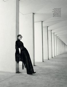 a woman is leaning against a column wearing sunglasses and a long black dress with fringes