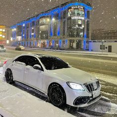 a white car parked in front of a building on a snow covered street at night