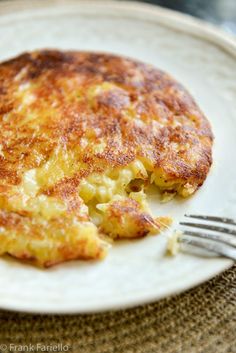 a white plate topped with an omelet and a fork on top of a table