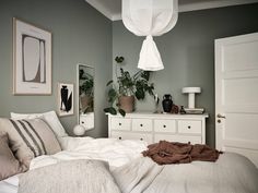 a white bed sitting in a bedroom next to a dresser and potted plant on top of it