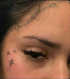 a woman's left eye with small stars on her forehead and behind her ear