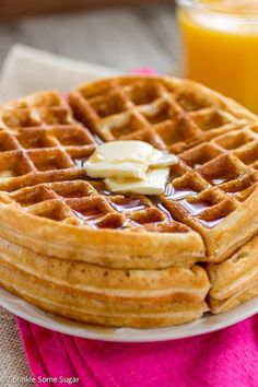 a stack of waffles on a plate with butter and syrup next to orange juice