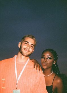 a man and woman standing next to each other in front of a dark sky at night