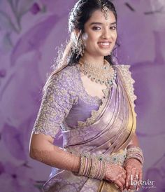 a woman in a purple and gold sari with jewelry on her neck, smiling at the camera