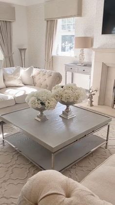 a living room filled with white furniture and flowers on top of a coffee table in front of a fire place