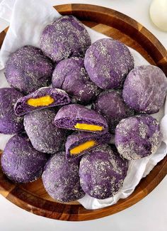 a wooden bowl filled with purple donuts covered in powdered sugar and orange peels