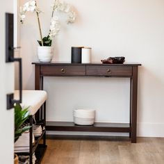 a wooden table topped with white flowers next to a vase filled with flowers on top of a hard wood floor