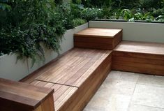 a wooden bench sitting on top of a tiled floor next to a planter filled with green plants