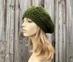 a mannequin head wearing a green crochet hat on top of a wooden fence