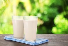 two glasses of milk sitting on top of a wooden table next to a blue towel