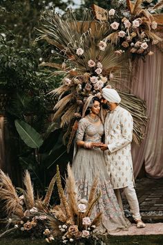 two people standing next to each other in front of a flower covered arch with flowers on it