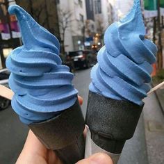 two ice cream cones with blue icing are held up in front of the camera