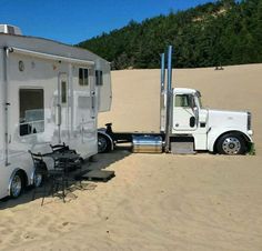 a white truck parked next to a trailer on top of a sandy beach with trees in the background