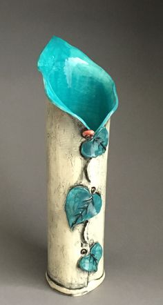 a silver and turquoise vase with flowers on the inside is sitting on a gray surface