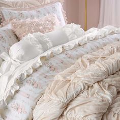 an unmade bed with ruffles and pillows on it in a pink room