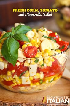 a salad with tomatoes, corn and basil in a glass bowl on a wooden table