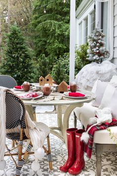 a table and chairs on a porch with christmas decorations in the back yard, along with red rain boots