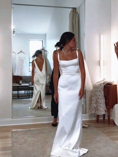 a woman standing in front of a mirror wearing a white dress