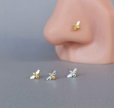 three small gold and silver bee studs sitting on top of a grey surface next to each other