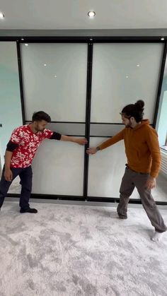 two young men are holding hands in front of an open glass door that is on the floor