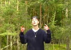 a man standing in the middle of a forest holding his hands up with two fingers