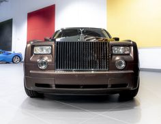 the front end of a brown rolls royce parked in a garage with two blue sports cars behind it