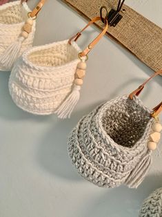 three crocheted baskets hanging from hooks on the wall with wooden beads attached to them