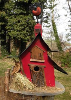 a red birdhouse sitting on top of a tree stump next to a pile of hay