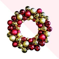 a red and gold christmas ornament wreath on a pink background with diagonal stripes