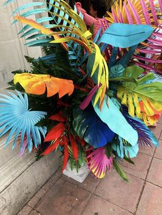 a vase filled with lots of different colored paper flowers and leaves on top of a brick floor