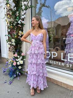 a woman standing in front of a store window wearing a purple tiered dress and sandals