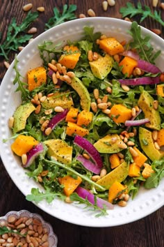 a salad with avocado, carrots and pine nuts in a white bowl