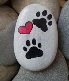 a painted rock with paw prints and a red heart on it, surrounded by gray rocks