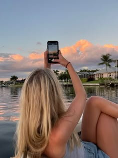 a woman sitting on the back of a boat while holding up her cell phone to take a photo