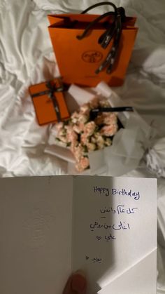 a hand holding an open birthday card next to some flowers on a white sheeted bed