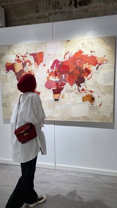 a woman walking past a large map in an art gallery with red and white colors