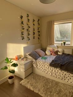 a bed room with a neatly made bed next to a window and a potted plant