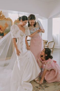 two women in wedding gowns and one is helping another woman put on her veil