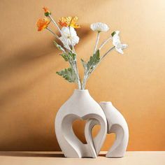 two white vases with flowers in them sitting on a table next to a wall