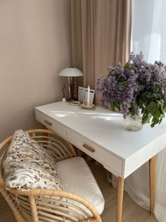 a wicker chair sitting next to a white desk with flowers on top of it