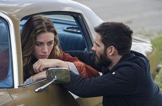 a man and woman leaning out the window of a car looking into each other's eyes