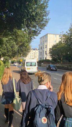 three girls walking down the street with their backpacks on and one girl talking on her cell phone