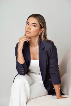 a woman sitting on top of a white couch wearing a blue blazer and white pants