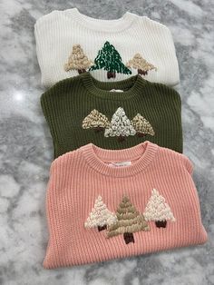 three sweaters with trees on them sitting on a marble surface