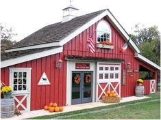 a red barn with pumpkins and hay bales in the front yard on a farm